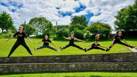 Jason TUESDAY - Five young people wearing black tshirts jump out from being a stone wall in Swanage