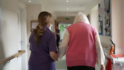 Big Mountain Productions/BBC Natalie walking with Jeanne to the dining room, holding hands, walking down a corridor 