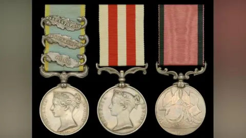 The image shows three historic military medals displayed side by side against a plain black background. Each medal hangs from a coloured ribbon and is suspended from a metal bar.