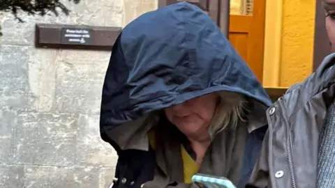 PA Jane Barnard looks to the ground as she leaves Gloucester Crown Court, her face is obscured by the navy blue hood of a rain jacket.