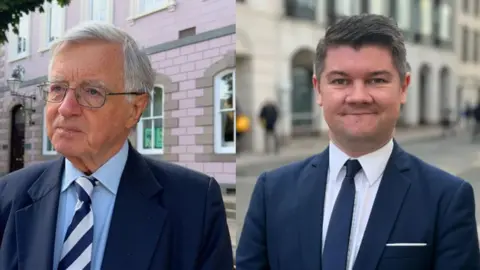 Deputies Sir Philip Bailhache and Sam Mezec both wearing blue suits and light coloured shirts. 