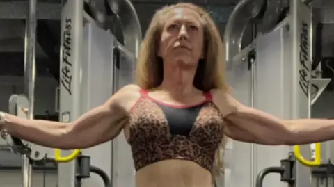 Jane Bennett Jane Bennett training at the gym. She is stood flexing her muscles at a workout machine.