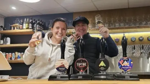 Two people smile widely behind a bra with drinks in the background