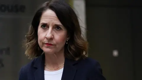 Liz Kendal in a dark suit and white top with a serious look on her face