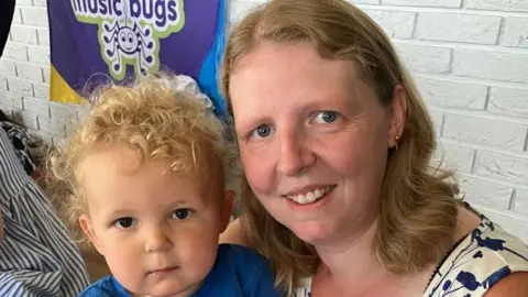 A woman with ginger hair in a blue and white patterned top with a small child with ginger curly hair
