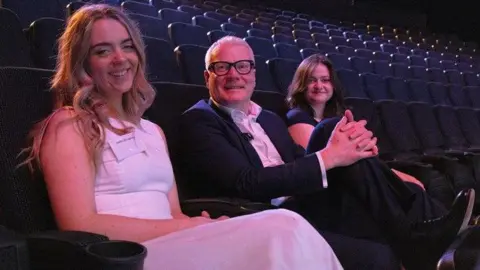 Jodie Boughey, Richard Parker and Sophia Kendal sat in an auditorium smiling a the camera