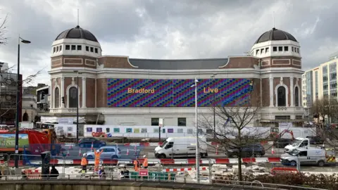 BBC A photo of a large building building made of red brick and white stone. There are two round towers at each end connected by a central section bearing the words Bradford Live
