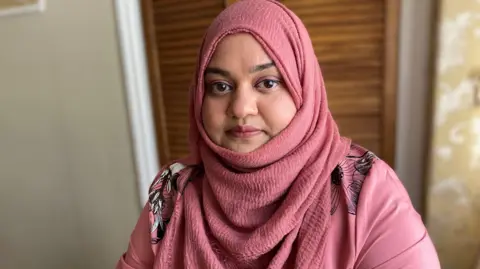Sahdia looking into the camera. She is wearing a pink hijab and pink top.