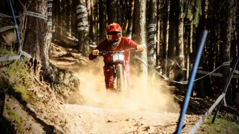 A downhill trail bike rider heading towards the camera with a cloud of dust