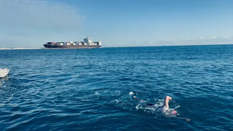 Prem's support crew Premal Pattani formerly from Swindon swimming in the Channel with an enormous cargo ship on the horizon behind him.