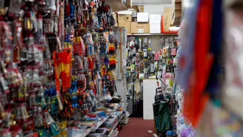A photograph showing the interior of the Lights and Gifts store, showing shelves of hardware items and tools such as saws, screwdrivers and paintbrushes. 