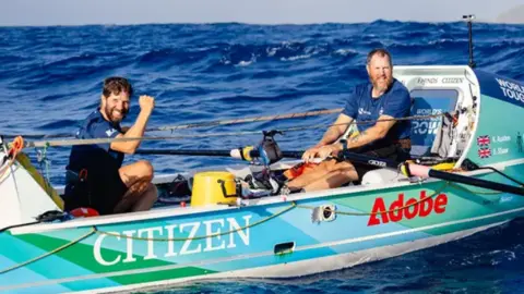 2Stroke.team Karl Austen and Ed Shaw in there rowing boat smiling at the camera. 