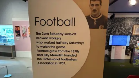 Sign at museum. It reads: 'Football. The pm Saturday kick-off allowed workers who worked half day Saturdays to watch the game. Football grew from the 1870s and Billy Meredith founded the Professional Footballers' Association in 1907.