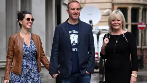 Reuters Tom Hayes smiles in the centre of the photo, between his lawyer and another woman.