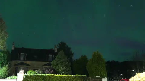 Green waves of Northern Lights capable    the entity  implicit    a cottage surrounded by trees