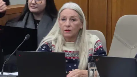 Paul Moseley/BBC Kay Mason-Billig sitting at a desk during a council meeting. She has long blonde/white hair.