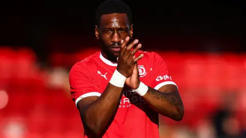 A black footballer in a red shirt applauds fans