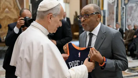 EPA/Shutterstock Pope Leo XIV greets US filmmaker Spike Lee during a special audience with the World of Cinema, at the Apostolic Palace, Vatican City. Lee hands him a New York Knicks shirt printed with 14 and "Pope Leo".