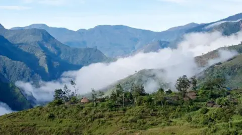 Fog rolling over green mountains, with some huts poised on a ridge