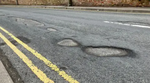 Two yellow lines next to a pockmarked road full of wide potholes.
