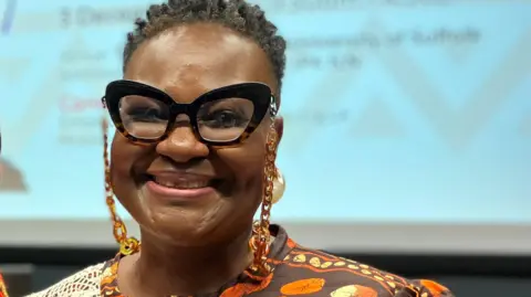 Valerie wearing glasses, with short dark hair, beams at the camera 