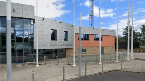The entrance to Gateshead Stadium. It has grey cladding with the words "Gateshead International Stadium" on it and glass windows. The right-hand side of the building is made from brick.