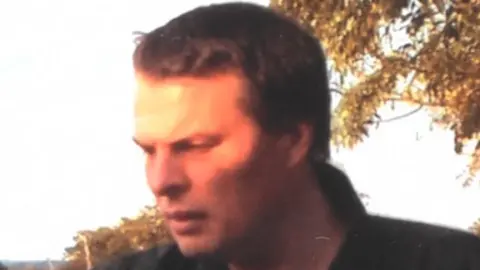 Darren Round pictured with brown hair wearing a blue and white stripe collar tshiret and dark jacket.