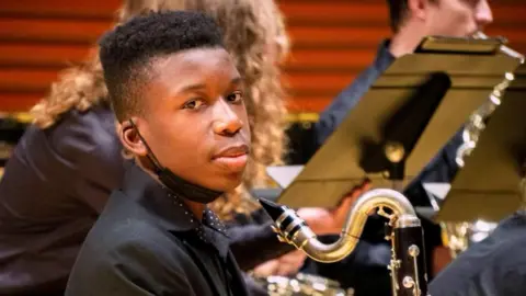 Reuters A young black boy sits in a chair and holds a clarinet during a school orchestra performance