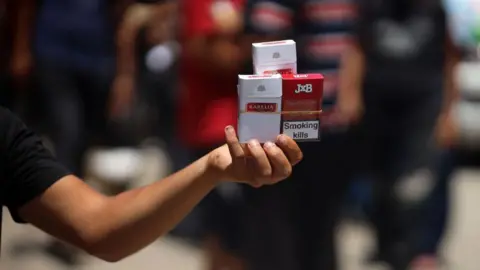 NurPhoto via Getty Images File photo showing a Palestinian man selling cigarettes on a street in Deir al-Balah, in the central Gaza Strip, on 12 June 2024