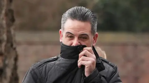 East Anglia News Service Christopher Nunn wearing a black coat. He is pulling the collar up to hide part of his face. He has short, slicked-back black and grey hair.