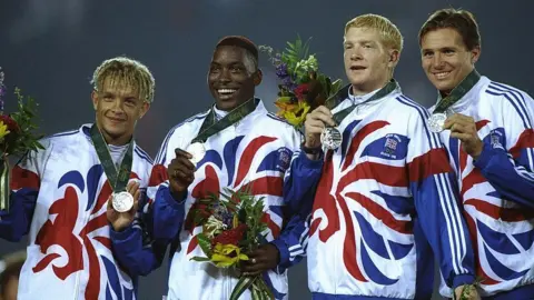 Getty Images Iwan Thomas second from the right holding his silver medal alongside his teammates. They are all wearing their Team GB tracksuits.