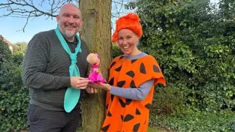 Shivani Chaudhari/BBC A man and woman dressed as the popular cartoon characters from The Flintstones. They are both smiling at the camera and standing by a tree 