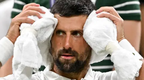 Novak Djokovic holds an ice towel on his head at a change of ends