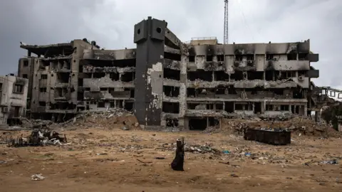 EPA Seorang wanita berjalan di antara puing-puing Rumah Sakit Al-Shifa yang rusak di Kota Gaza, Gaza Utara (5 Februari 2025)