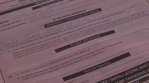 A pink inspection form, filled in in pencil, says the boiler is "immediately dangerous" with the cause being "found flue letting by POCs"