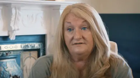 Retirement Editor A woman with long blonde hair and blue eyes looks to the left of the camera and sits in a chair. There is a fireplace behind it.