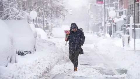 A person walks through a snow filled street carrying a bundle of pink flowers