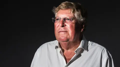 Getty Images Edward Stourton attends a photocall during the annual Edinburgh International Book Festival at Charlotte Square Gardens in 2018. He is standing alone against a dark background.