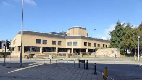 Southampton Crown Court, a blocky concrete building next to a main road junction. It's a sunny day and the sky is blue.