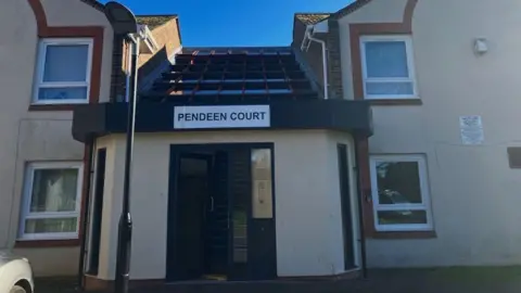 Pendeen Court's exterior - a white two-storey building with the name 'Pendeen Court' written on a white sign above the black front door