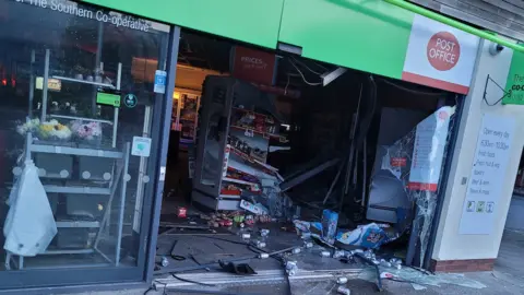 A Co-op shop window and door is smashed and debris is on the ground after a ram raid.
