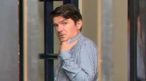 BBC Michael McMonagle wearing a chequered shirt and holding his collar.