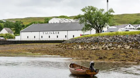 The white-walled distillery buildings with a small wooden boat, fitted with an outboard engine, in the foreground.