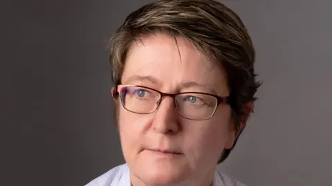 Leigh Day A woman with short brown hair who is wearing glasses and looking to one side of the camera.