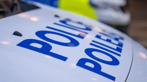 A white police vehicle bonnet with the word 'POLICE' in bold blue lettering on it.