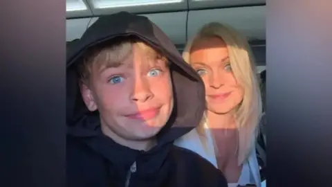 Family handout Mikey Roynon (L) has blonde hair and is wearing a black hoodie. He is pictured smiling in a selfie next to his mother Hayley, who has long blonde hair and is wearing a white top. 