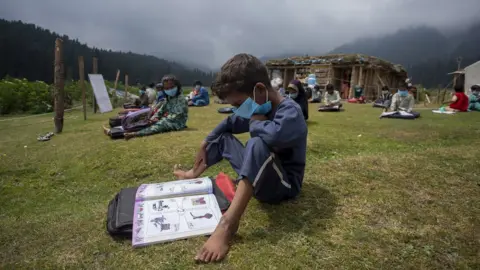 BBC A boy reads a book during a class in the outdoors.