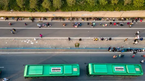 Getty Images Foxconn workers resting on one side of a highway and two buses parked on the other side