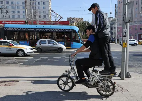 Getty Images Two work migrants from Kyrgyzstan ride bicycle on the street, April,14,2023, in Moscow, Russia.