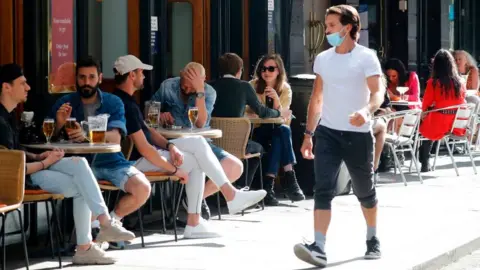 Getty Images Man walking past people drinking outside a bar